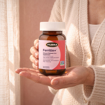 A woman's hands holding a bottle of Ferritin+ on her open palm in warm afternoon light
