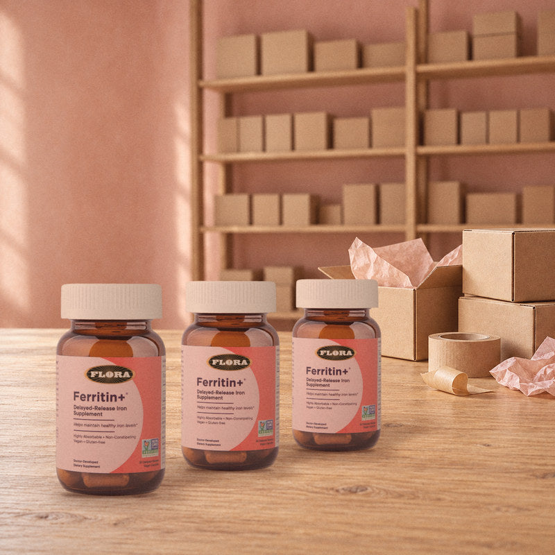 Three bottles of Ferritin+ on a wooden packing table with shipping boxes, in warm light